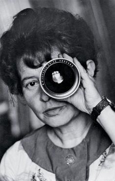 an old black and white photo of a woman holding a camera up to her face