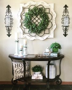 a table with some plants on top of it next to a wall mounted wreath and candles