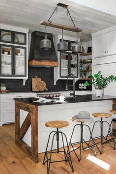 a kitchen with white cabinets and wooden stools in front of an island that has black counter tops