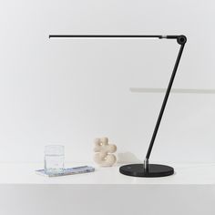 a desk lamp sitting on top of a white table next to a glass of water