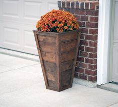 a wooden planter with orange flowers in front of a brick wall and garage door