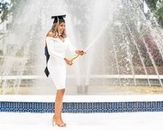 a woman in a graduation cap and gown is holding a water sprinkler