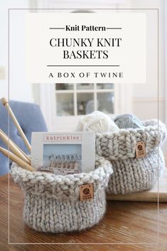 two knitted baskets sitting on top of a wooden table with knitting needles in them