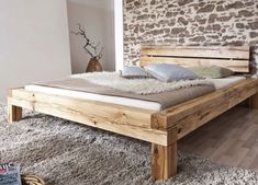 a wooden bed sitting on top of a white rug next to a wall covered in stone