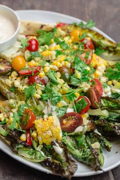 a white plate topped with corn, tomatoes and lettuce next to a bowl of ranch dressing