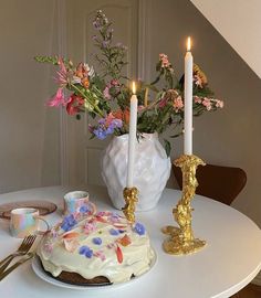 a white table topped with a cake covered in frosting next to a vase filled with flowers