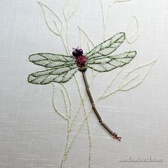 an embroidered dragonfly on white fabric with green stems and beads attached to it's wings