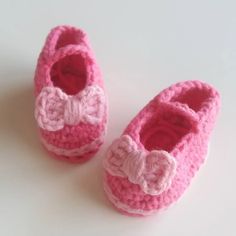 two pink crocheted baby shoes with bows on them sitting next to each other