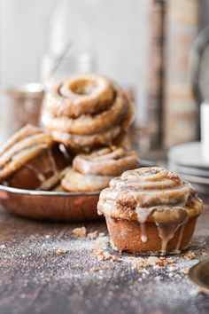 cinnamon rolls with icing sitting on a table next to a bowl of sugared doughnuts