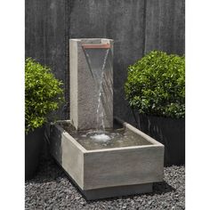 an outdoor fountain with water running from it's sides and plants in the background