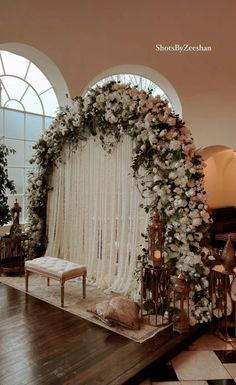 a wedding ceremony setup with white flowers and greenery on the wall, in front of two arched windows