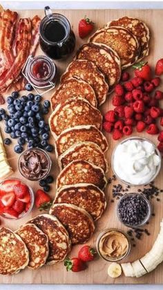 pancakes, strawberries, bananas, blueberries and other foods are arranged on a cutting board