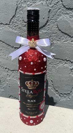 a bottle of red wine with a white ribbon on the top is sitting in front of a gray wall