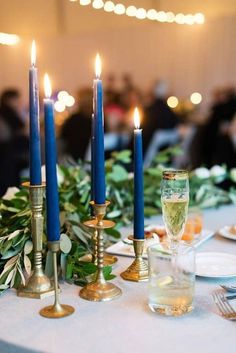 a table topped with candles and plates covered in greenery on top of a white table cloth