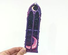 a hand holding up a purple sticker with the moon and stars on it, in front of a white background