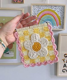 a hand holding a crocheted flower hanging from a wall with pictures on it