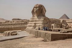 people are sitting at the base of an ancient sphinx in front of some pyramids