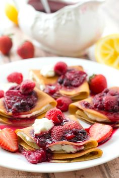 crepes with berries and whipped cream are on a plate next to lemon wedges