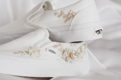 two white shoes with flowers on them sitting on top of a bed covered in white sheets