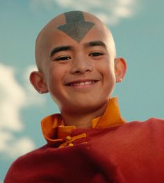 a young boy with a bald head and shaved hair smiles at the camera while wearing an orange shirt