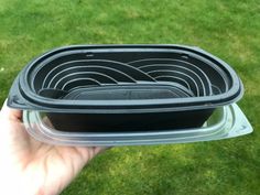 a hand is holding three black bowls on top of each other in front of some green grass