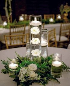 a table topped with candles and flowers on top of a white table cloth covered in greenery