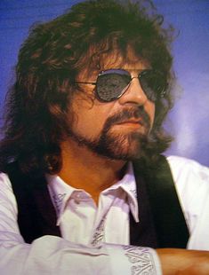 a man with long hair wearing sunglasses and a vest