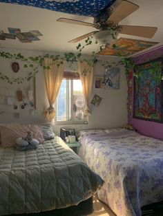 two beds in a room with paintings on the wall and ceiling fan above them,