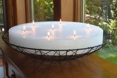 a white cake with lit candles in it on top of a wooden table next to a window