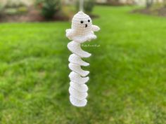 a white crocheted wind chime hanging from a string in the grass with a house in the background