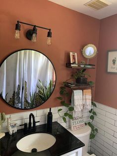 a bathroom with a black counter top and white tile walls, along with a round mirror on the wall