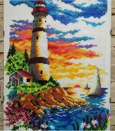 a cross stitch picture with a lighthouse and sailboat in the water at sunset on a stone wall