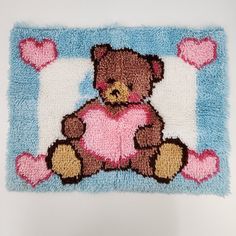 a teddy bear hooked up to a blue and white rug with pink hearts on it