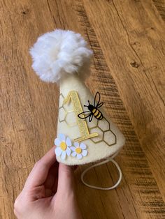 a hand is holding a small hat with a bee on it and daisies in the center