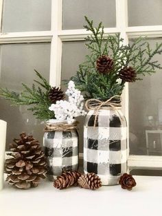 some pine cones are sitting next to two mason jars with christmas decorations on the windowsill