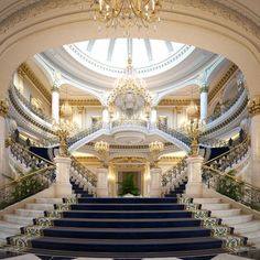 an ornate staircase with chandelier and blue carpeted steps leading up to the second floor