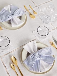 a white table topped with plates and silverware covered in blue striped bow napkins