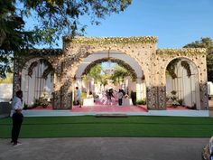 an outdoor ceremony with people standing in front of the arch and flowers on the ground