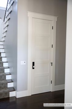 a white door in the middle of a room with stairs leading up to an upper floor