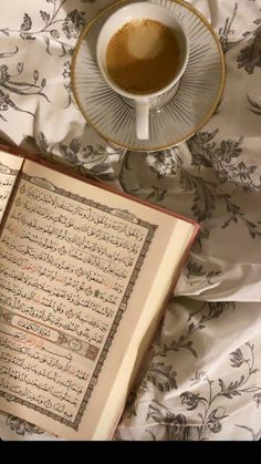 an open book with arabic writing on it next to a cup of coffee and saucer