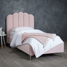 a bed with a pink headboard sitting on top of a wooden floor next to a table