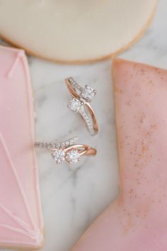 two diamond rings sitting next to each other on a marble surface with pink and white shapes