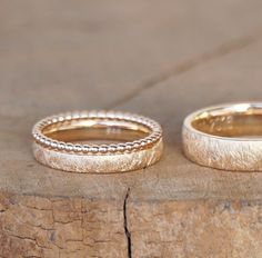 two gold wedding bands sitting on top of a piece of wood