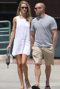 a man and woman are walking down the street holding hands while wearing white dresses, sunglasses and flip flops