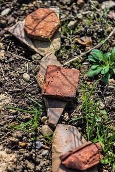 some rocks are laying on the ground near grass and dirt, with one rock sticking out of it's side