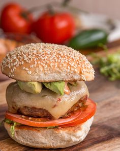 a cheeseburger with tomatoes, lettuce and tomato slices on a wooden cutting board