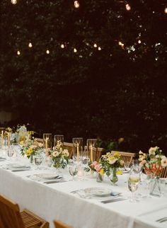 a long table is set with flowers and candles for an outdoor dinner party in the evening