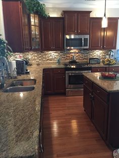 a kitchen with wooden floors and granite counter tops, stainless steel appliances and dark wood cabinets