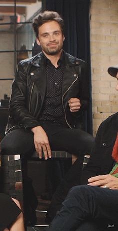 two men sitting next to each other in front of a brick wall and wearing hats