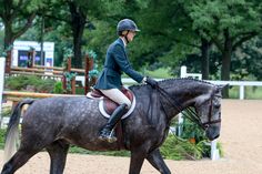 a woman riding on the back of a brown horse in an enclosed area with trees